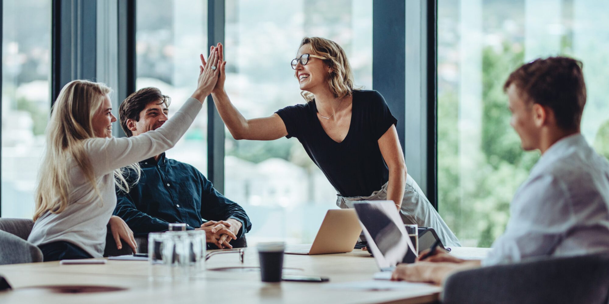 Female professional giving a high five to her colleague in conference room. Group of colleagues celebrating success in a meeting.